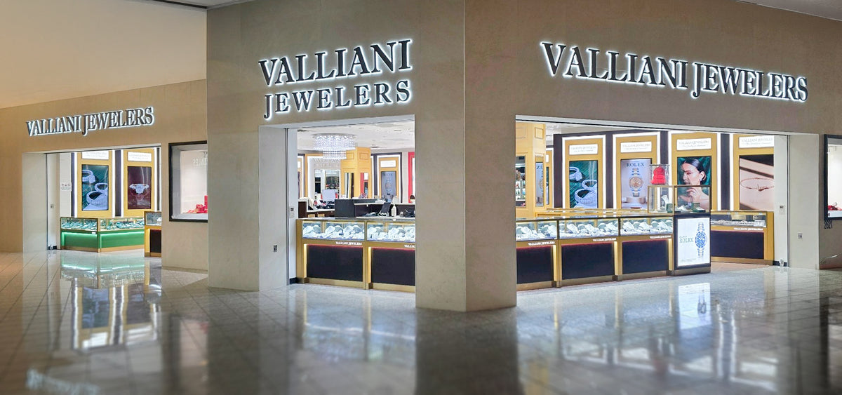 A store storefront for Valliani Jewelers inside a shopping mall, featuring illuminated signage, glass display cases filled with jewelry, and polished reflective floors.
