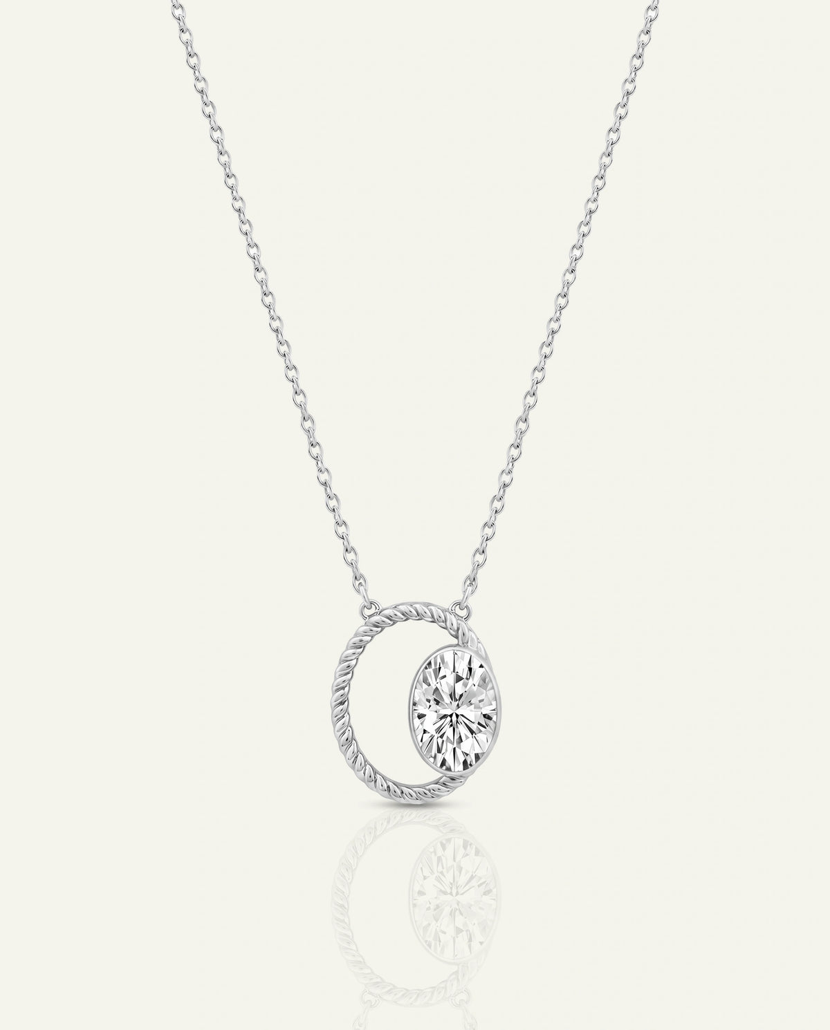 A silver necklace featuring a twisted oval pendant with a clear faceted gemstone, displayed on a light cream background with a soft reflection below.