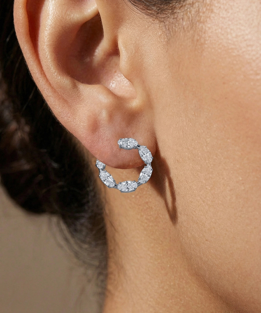 Close-up of a diamond hoop earring on an ear with a neutral background