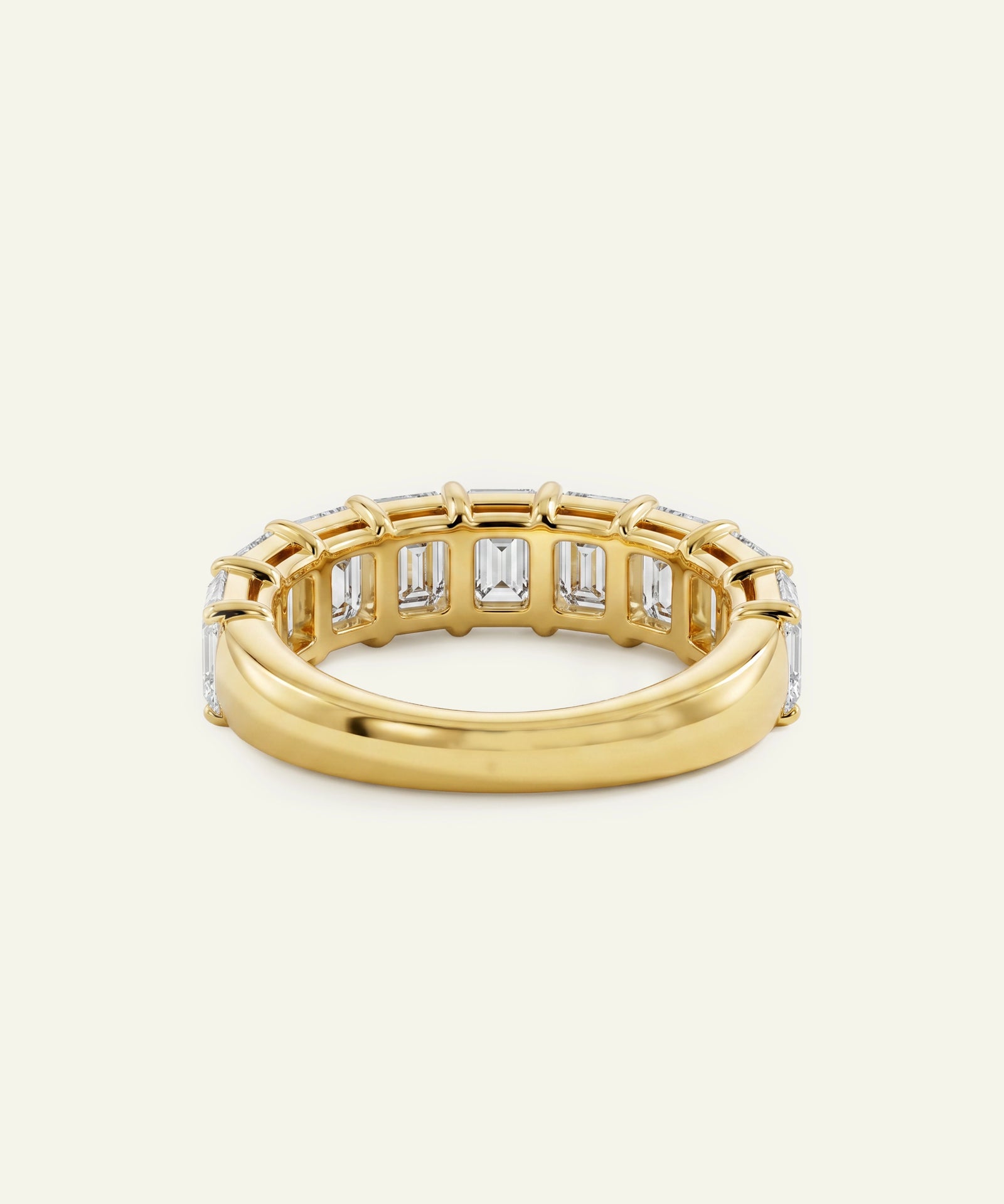 A yellow gold eternity ring featuring a row of baguette-cut clear stones, photographed on a light cream background.