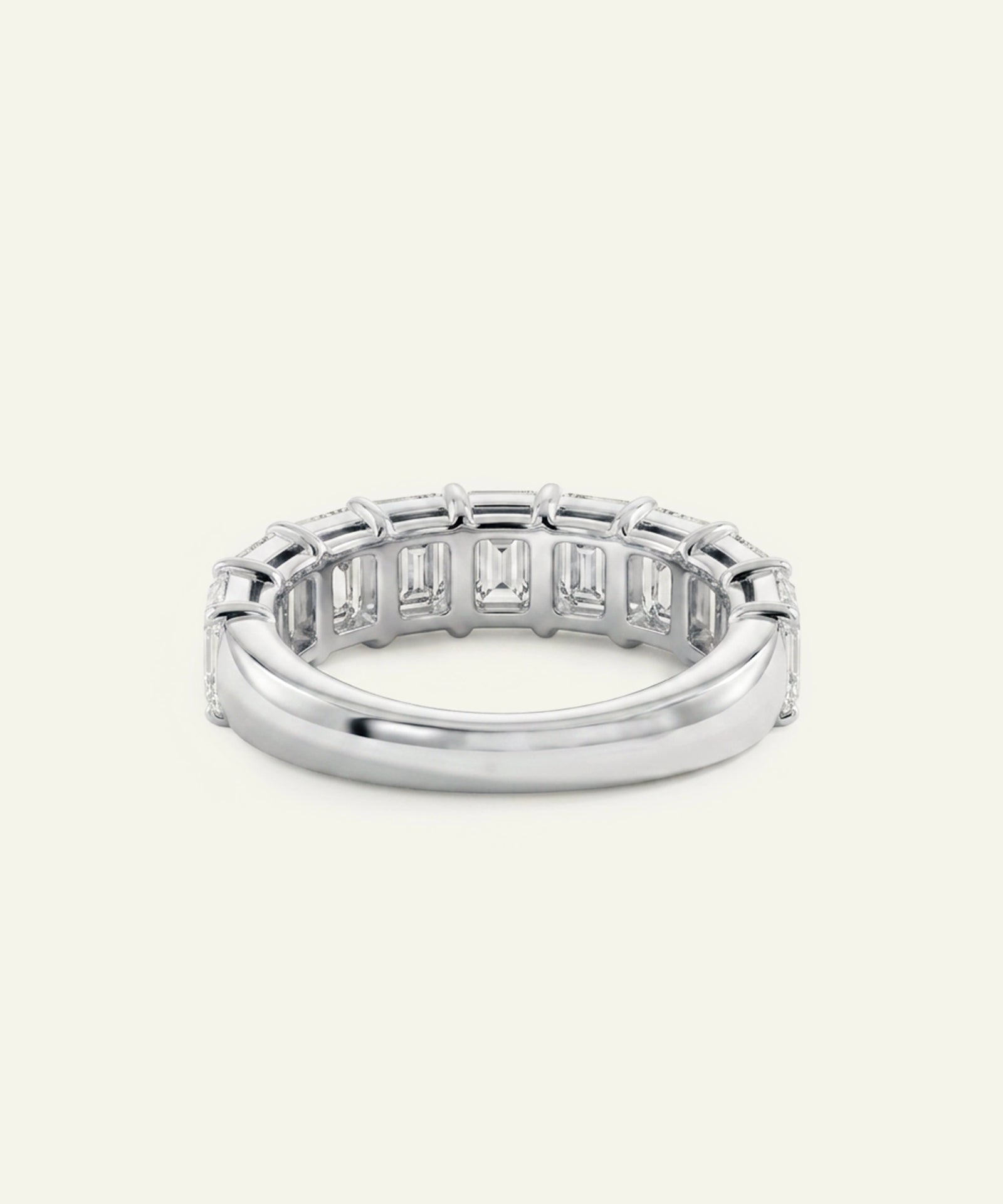 A silver tennis band ring featuring a row of baguette-cut clear gemstones on the outer side, shown against a light cream background.