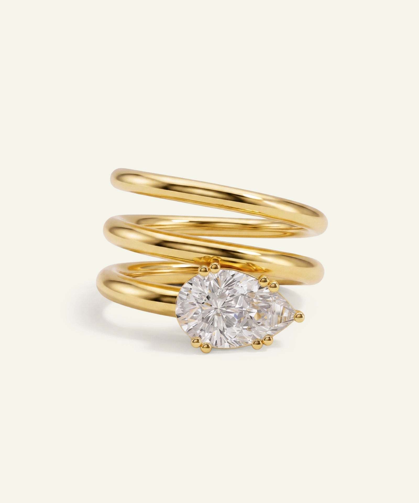 A gold spiral wrap ring featuring a large pear-cut diamond in a prong setting, photographed on a clean off-white background.