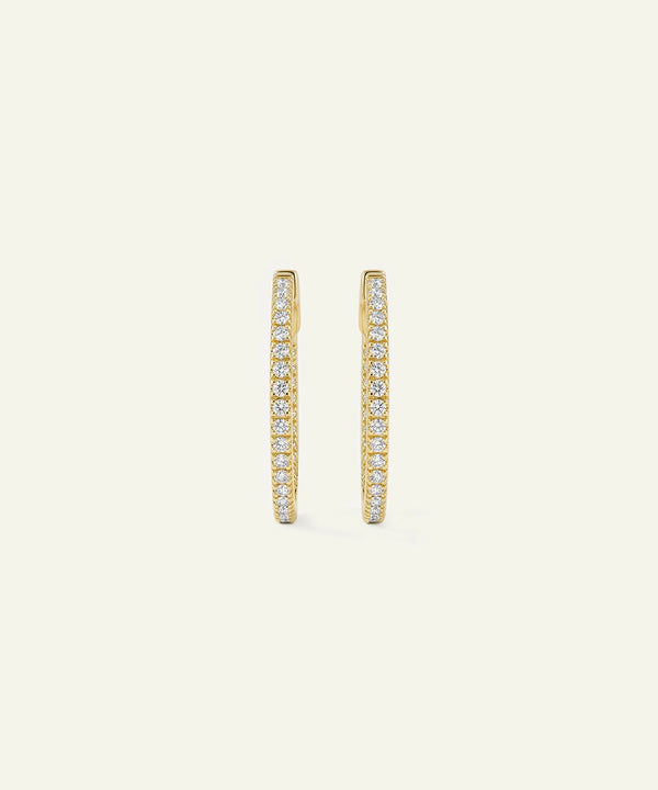 Gold hoop earrings with embedded stones on a light beige background