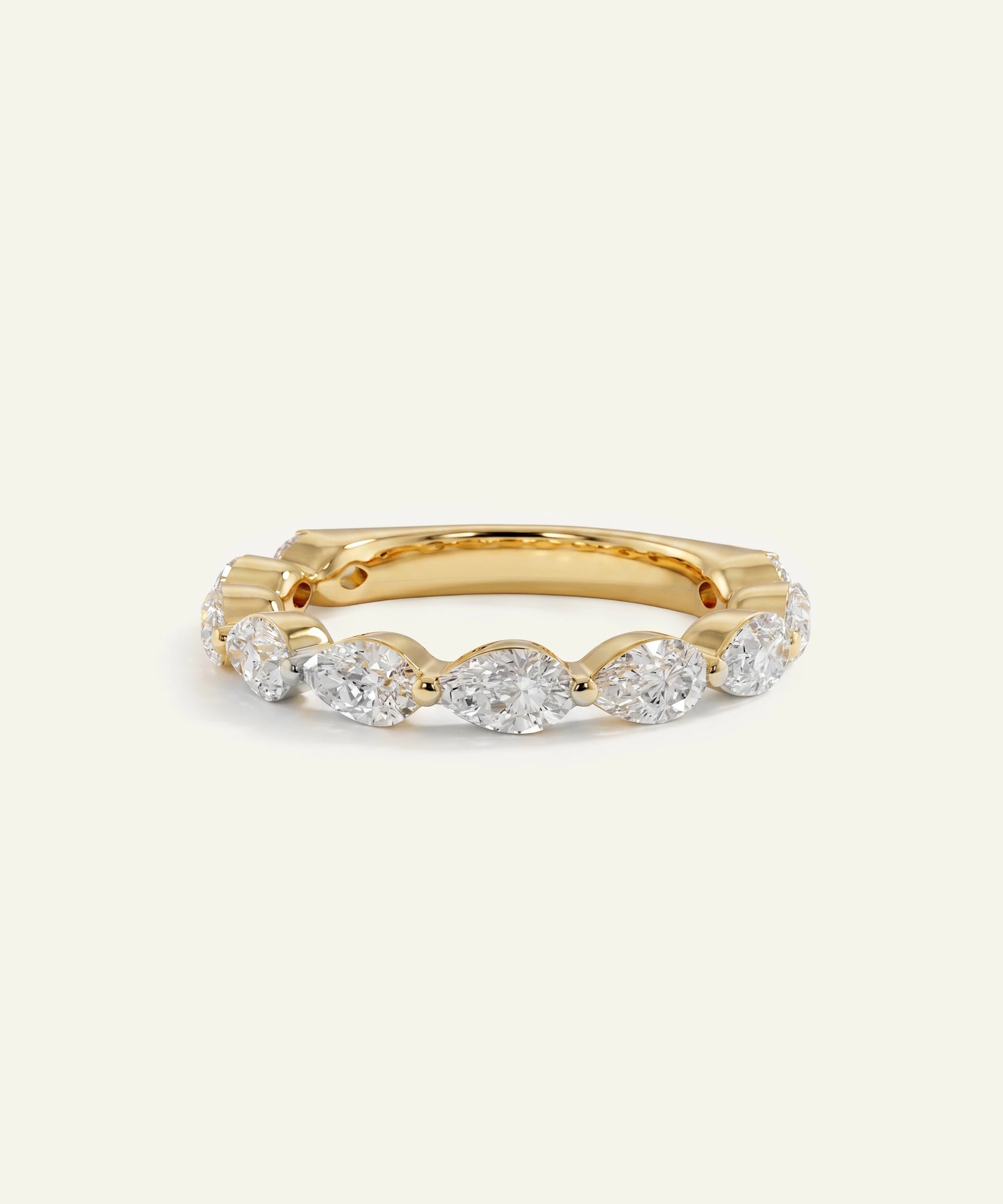 A yellow gold eternity ring featuring a row of round-cut clear gemstones, photographed on a clean, solid off-white background.