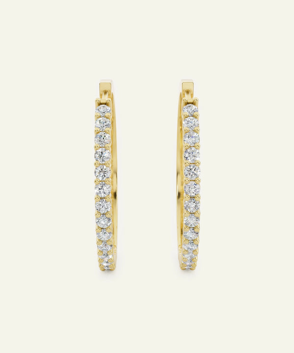 Gold hoop earrings with embedded diamonds on a light beige background