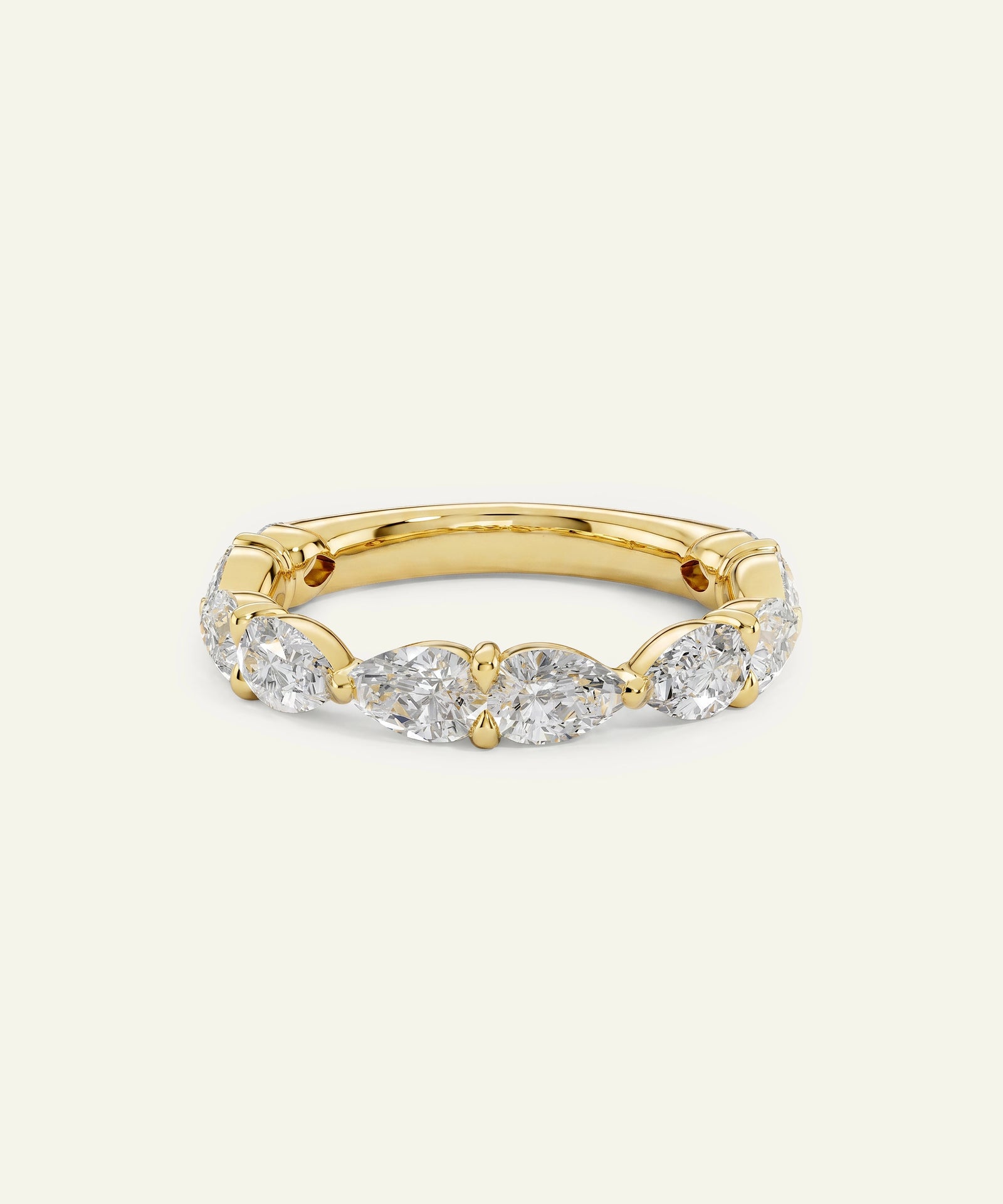 A yellow gold eternity ring featuring marquise-cut and round brilliant-cut diamonds, set against a solid off-white background.