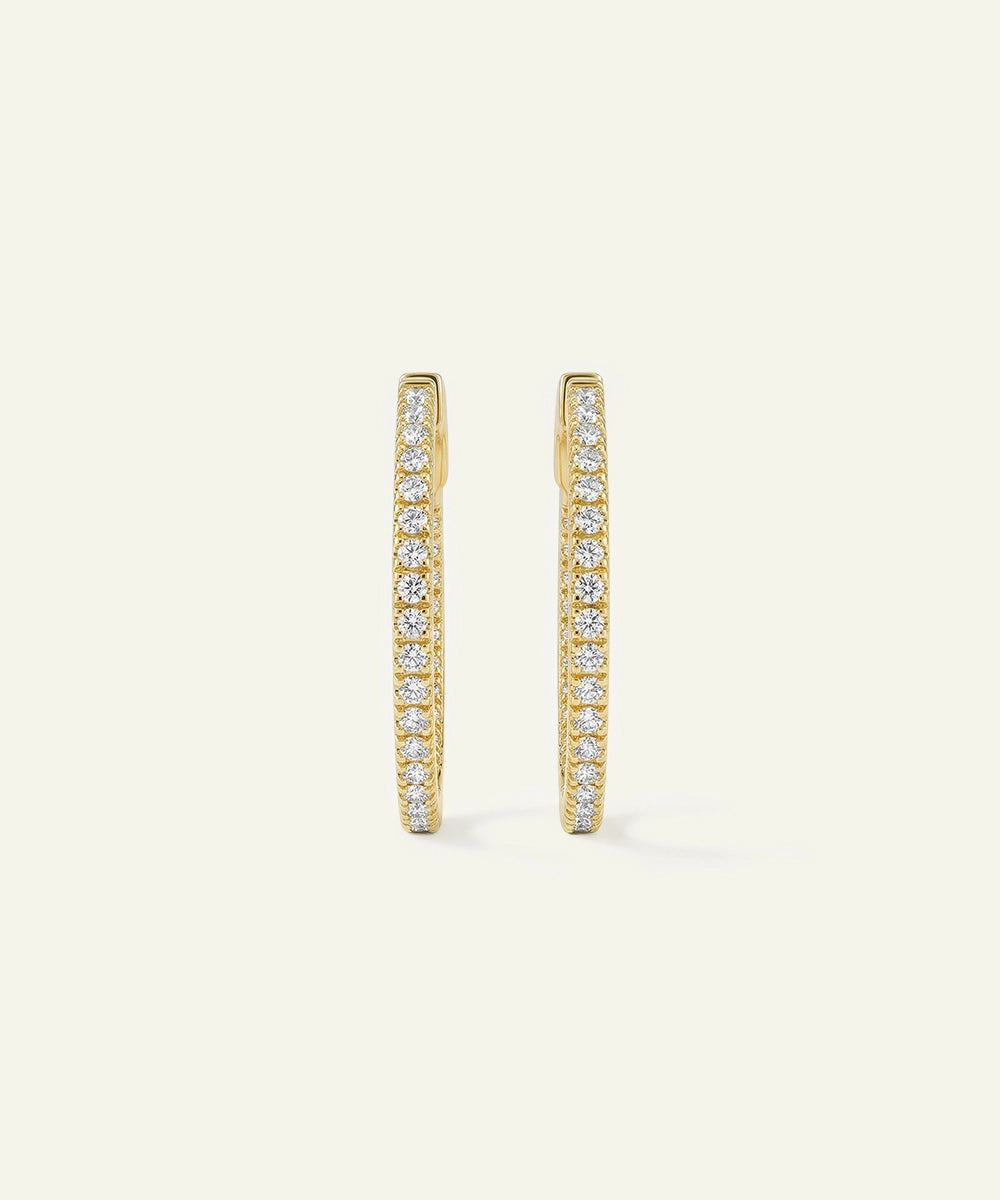 Gold hoop earrings with embedded diamonds on a light beige background