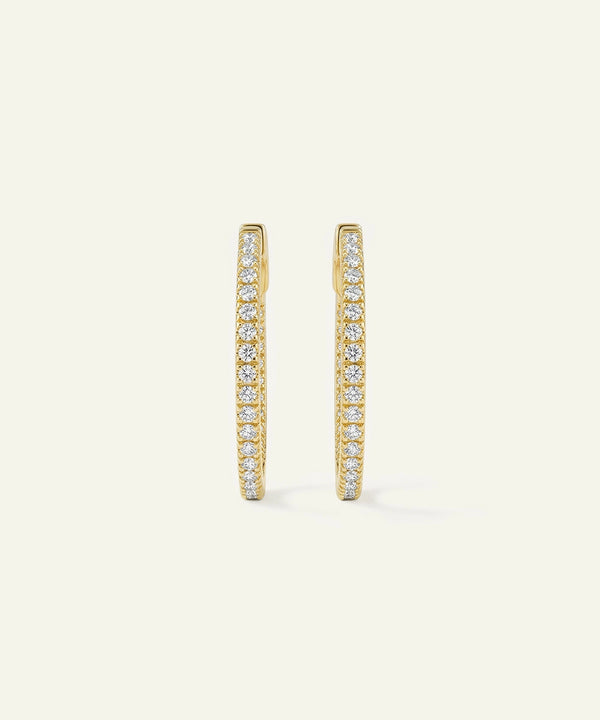 Gold hoop earrings with embedded diamonds on a light beige background