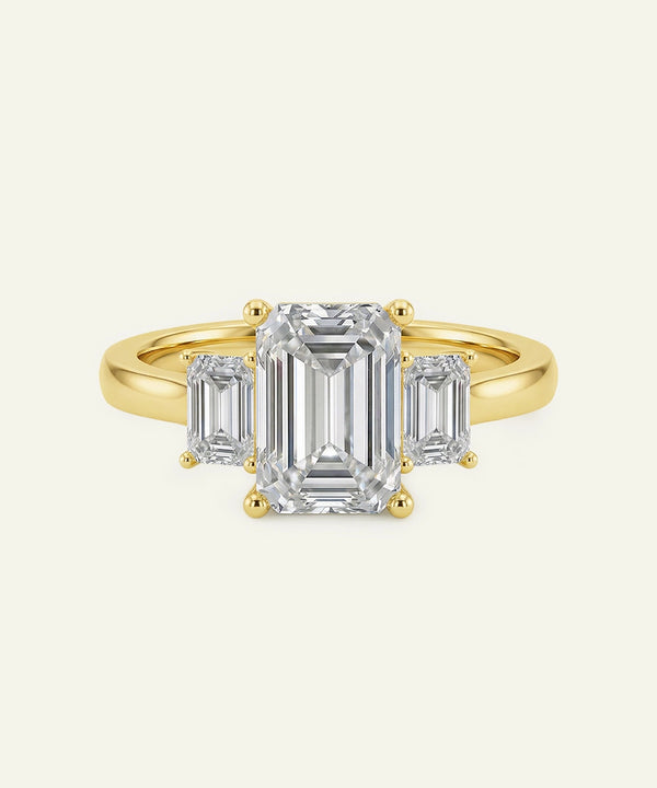 Gold ring with emerald-cut diamonds on a white background