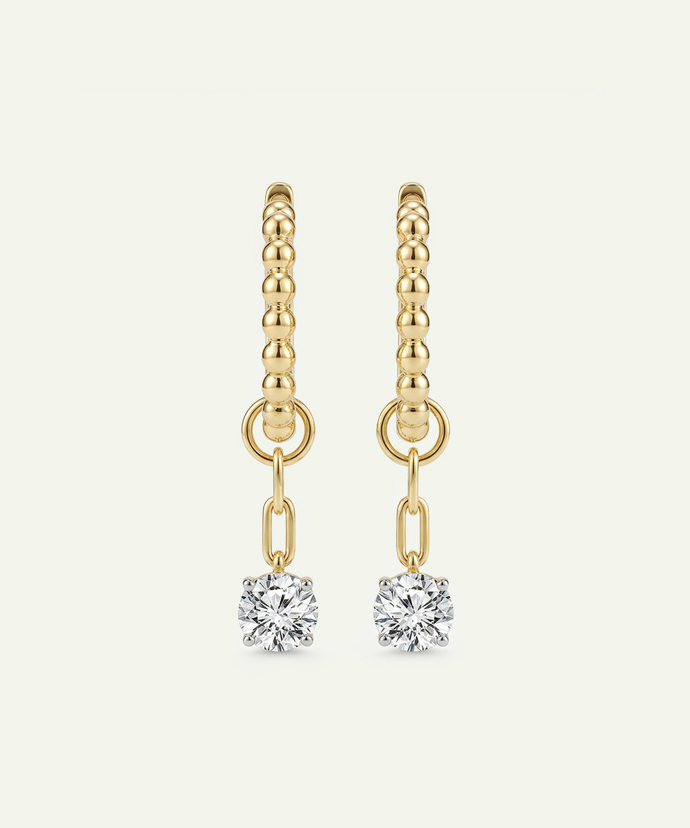 Gold earrings with diamond drops on a light beige background