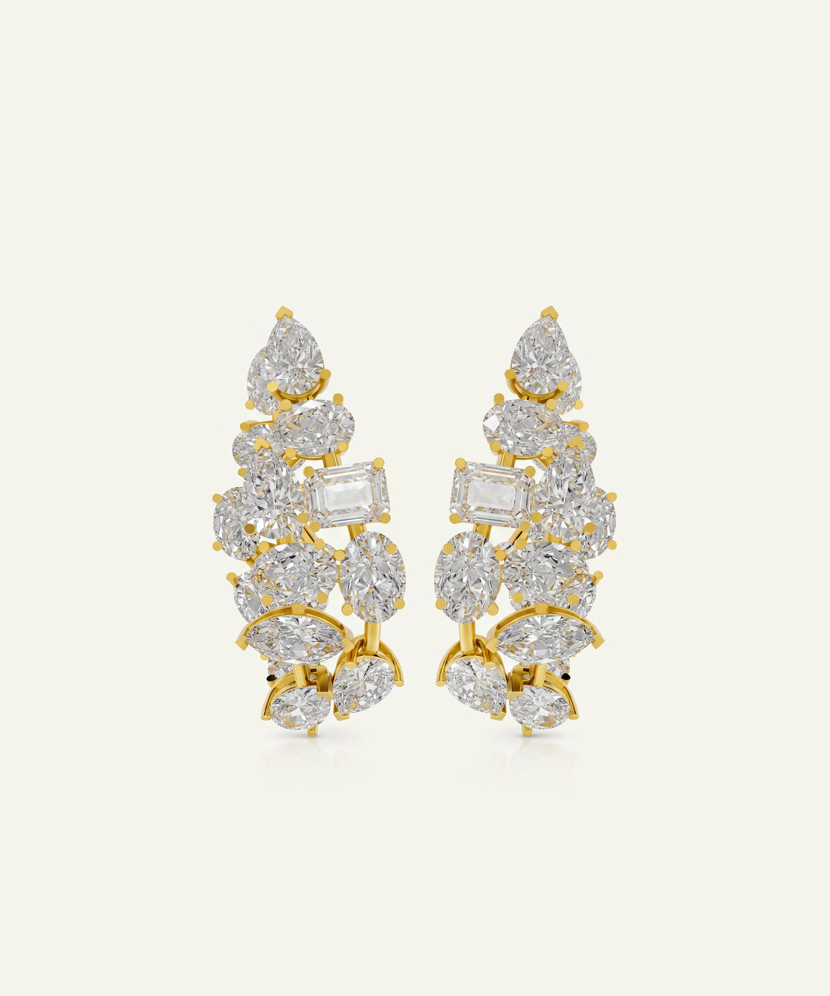 A pair of gold leaf-shaped earrings adorned with clear gemstones in pear, marquise, and baguette cuts, set against a solid off-white background.