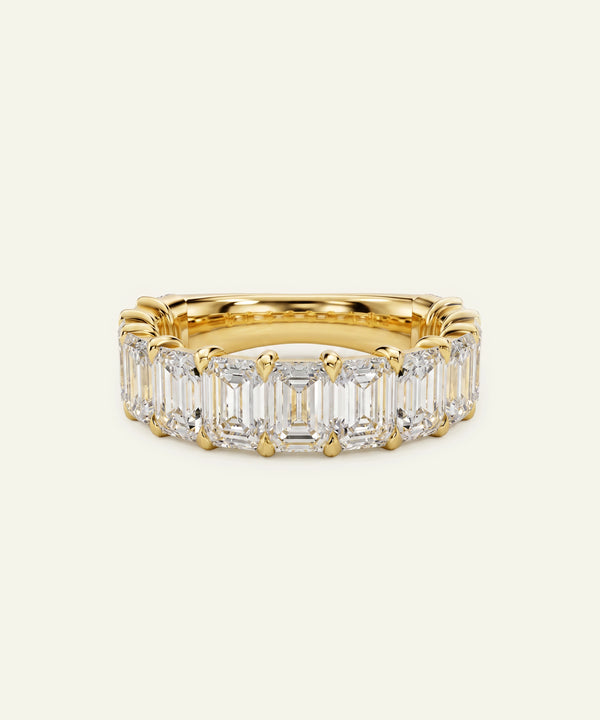 A yellow gold eternity ring featuring a row of baguette-cut clear diamonds, set against a plain off-white background.