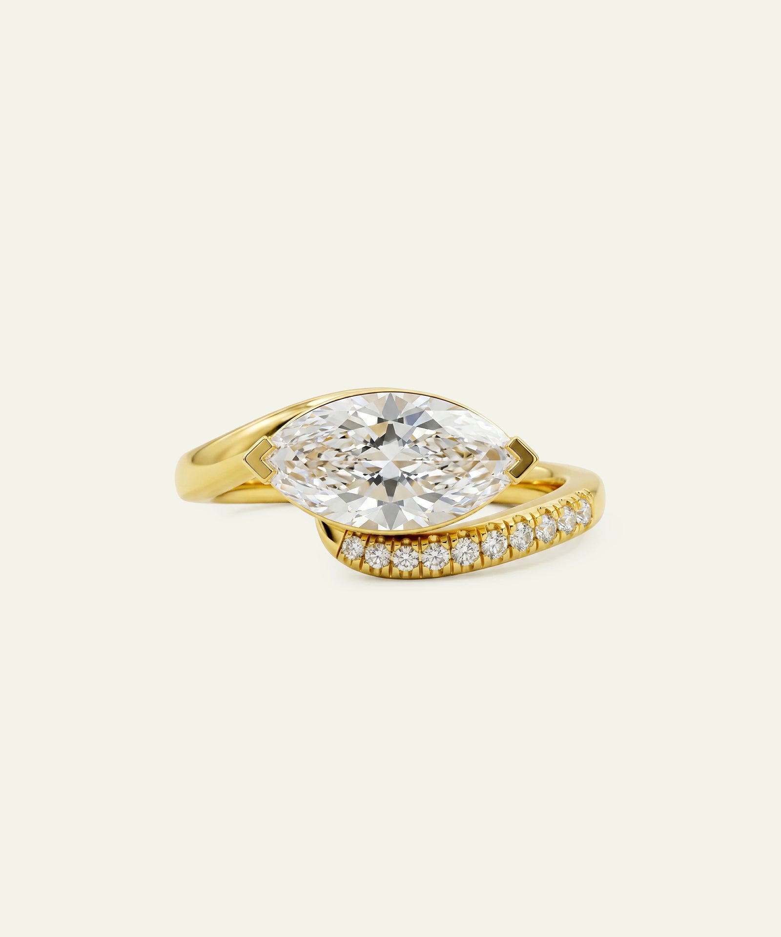 A yellow gold ring featuring a large marquise-cut clear center stone and a pavé-set band with small diamonds, shown on a light cream background.