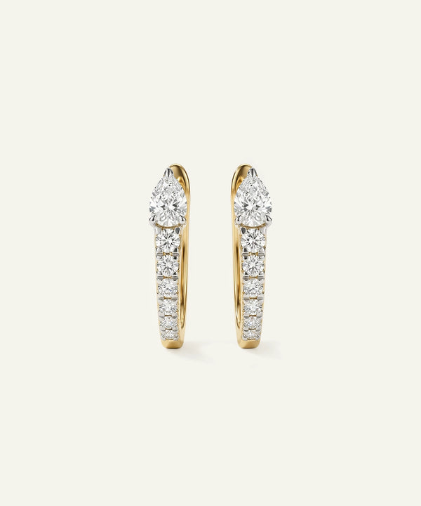 Gold hoop earrings with diamond accents on a light beige background