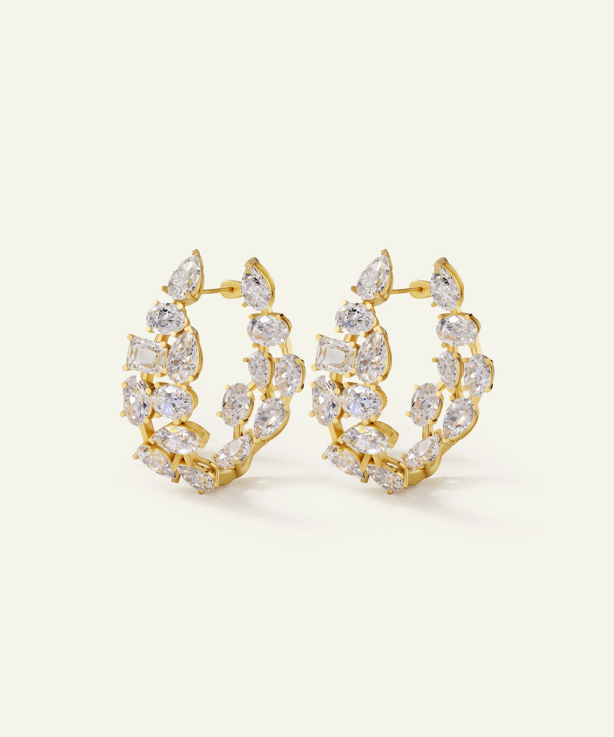A pair of gold hoop earrings adorned with marquise and round-cut clear crystals, displayed on a clean, light cream background.