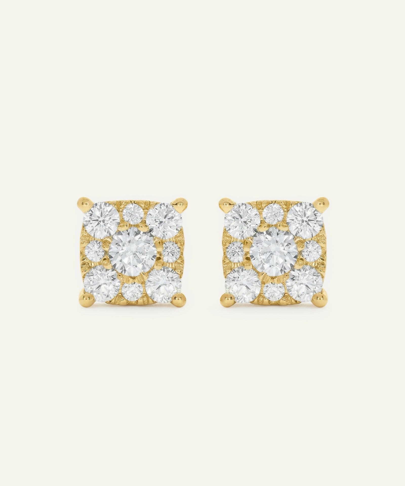 Pair of gold square-shaped earrings with clear gemstones on a beige background