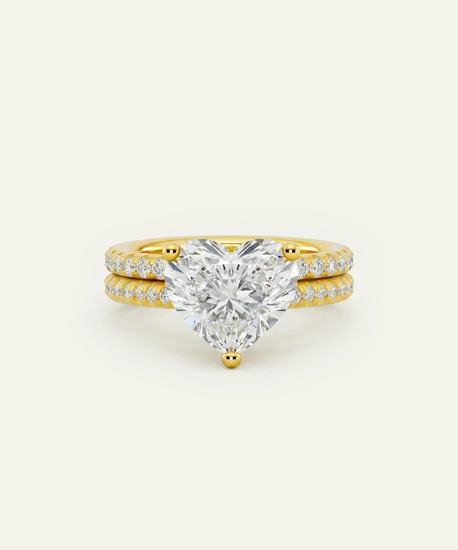 A yellow gold engagement ring featuring a large heart-shaped diamond center stone, flanked by two slim diamond-paved bands, set against a solid off-white background.