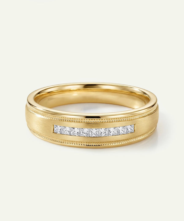 A men's yellow gold wedding band featuring a central row of channel-set princess-cut diamonds, accented by a brushed matte finish and fine milgrain beaded edges.