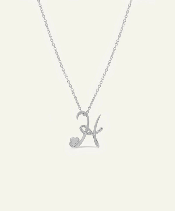 Silver necklace with a heart and letter 'K' pendant on a light gray background