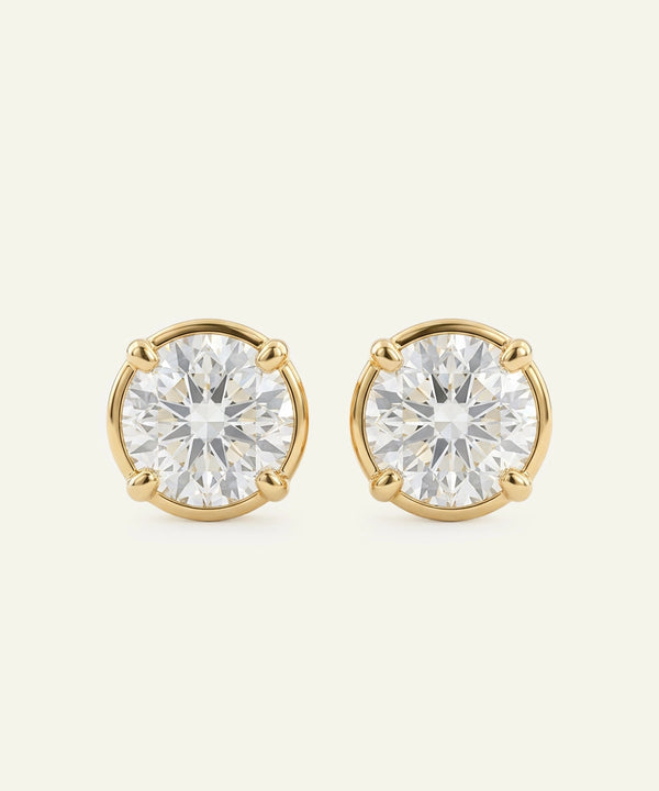 Pair of gold stud earrings with clear gemstones on a beige background