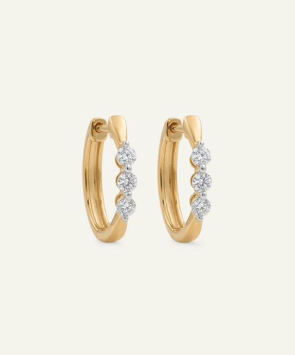 Gold hoop earrings with diamond accents on a light beige background