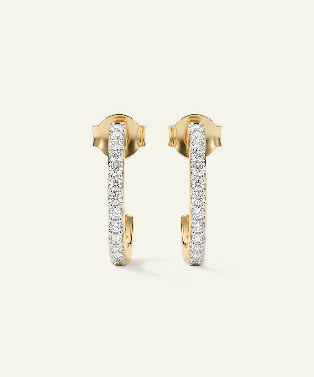 Gold hoop earrings with embedded diamonds on a light beige background