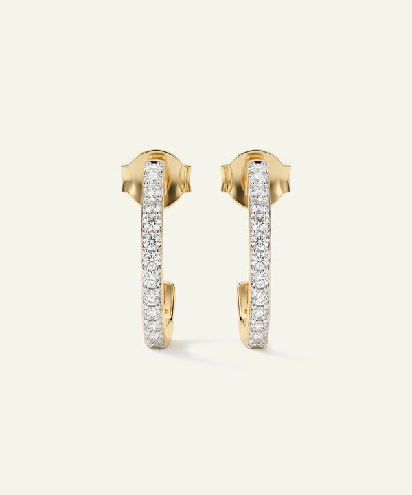 Gold hoop earrings with embedded diamonds on a light beige background
