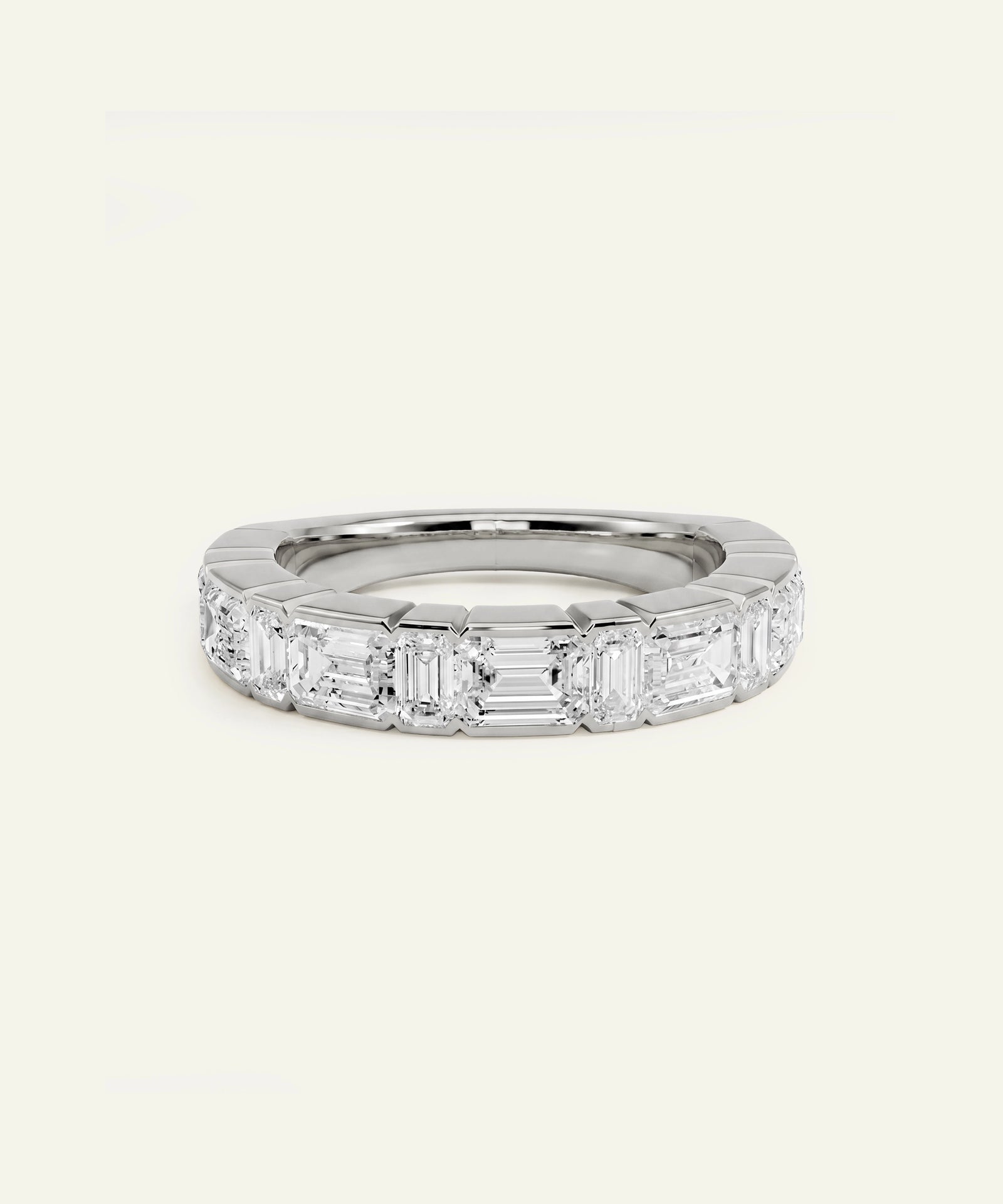A silver band ring featuring a row of baguette-cut clear gemstones, photographed on a clean, solid off-white background.