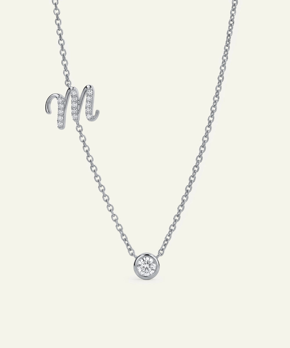 Silver necklace with a round pendant and 'M' letter on a light gray background