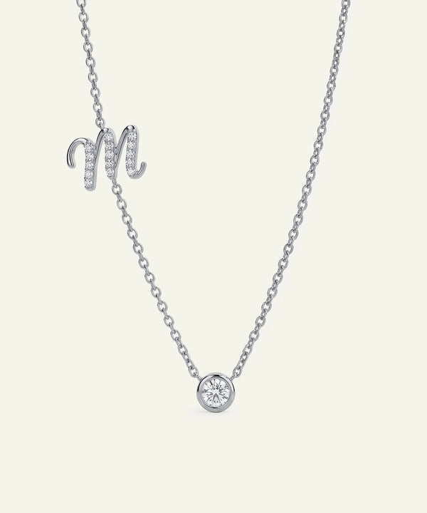 Silver necklace with a round pendant and 'M' letter on a light gray background