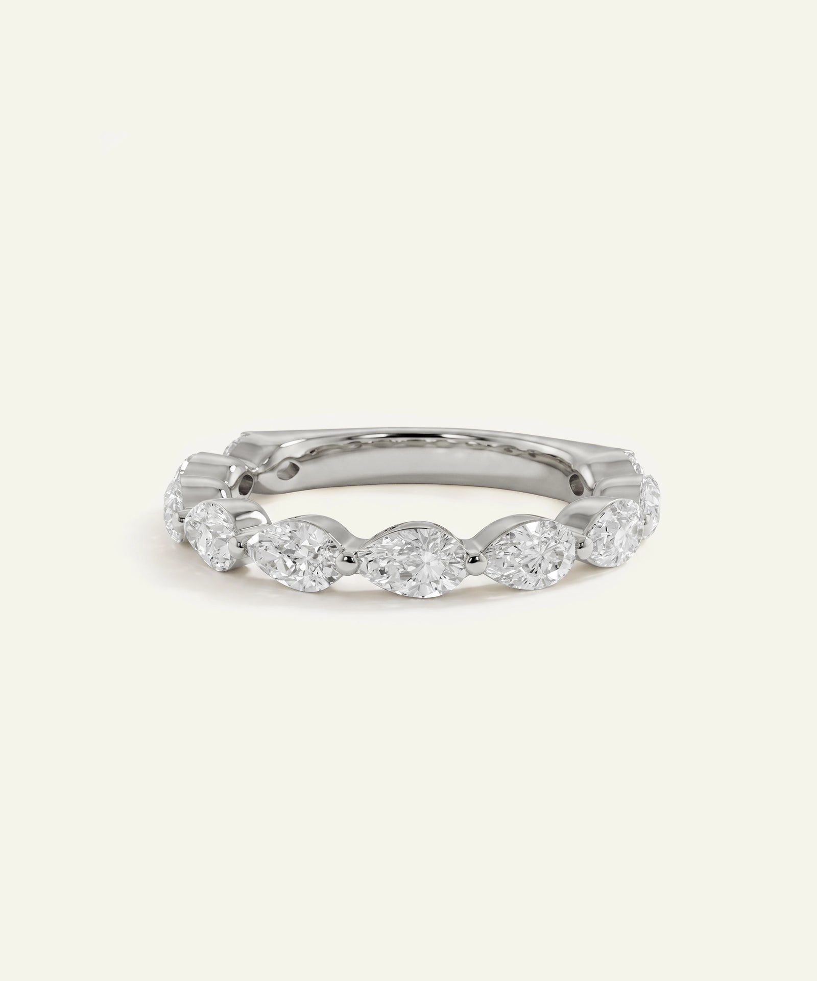 A silver-toned eternity ring featuring a row of round-cut clear gemstones in a beaded setting, photographed on a clean, solid off-white background.