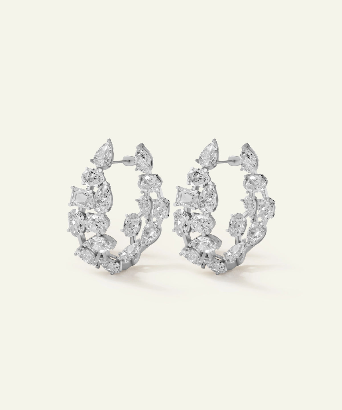 A pair of silver-toned hoop earrings adorned with marquise and round-cut clear gemstones, displayed on a clean, light cream background.