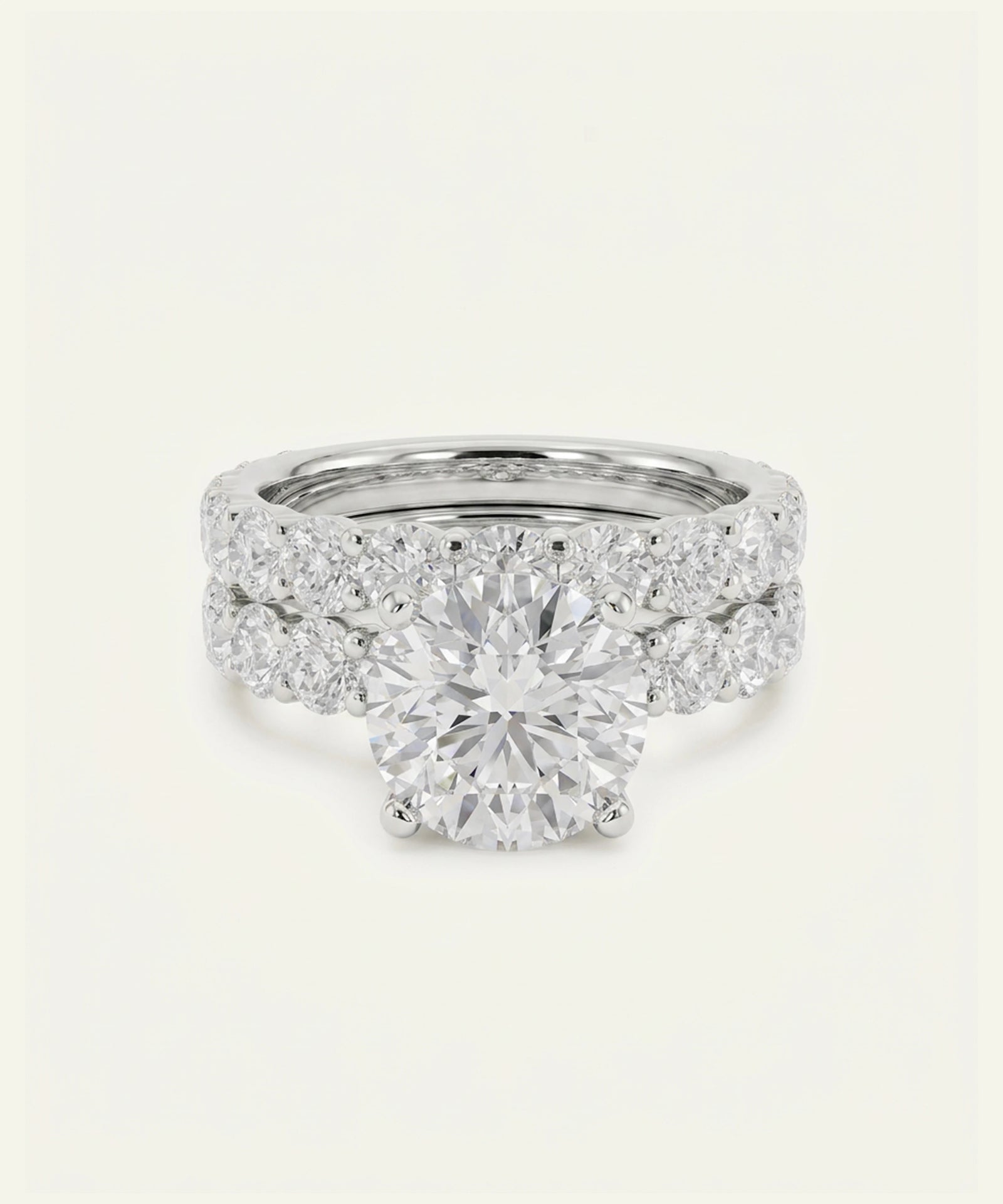 A diamond engagement ring with a round center stone and a pavé band, shown on a plain off-white background.