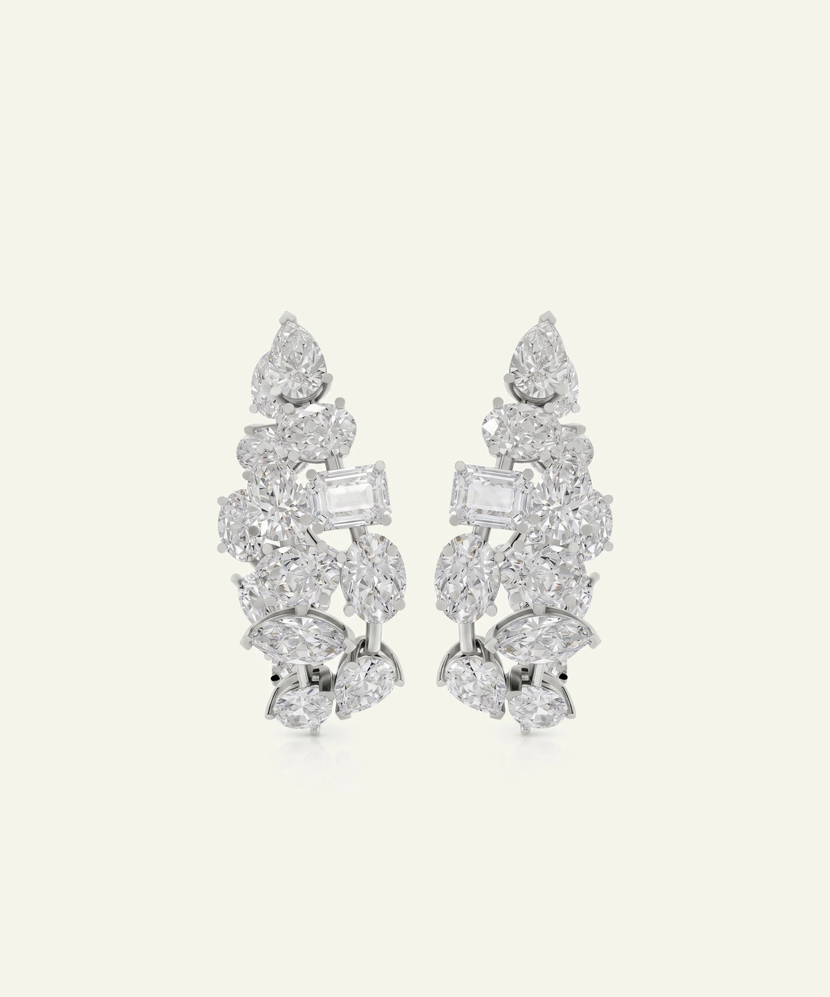 A pair of silver-toned leaf-shaped drop earrings set with clear gemstones, including pear, baguette, and marquise cuts, displayed on a light cream background.