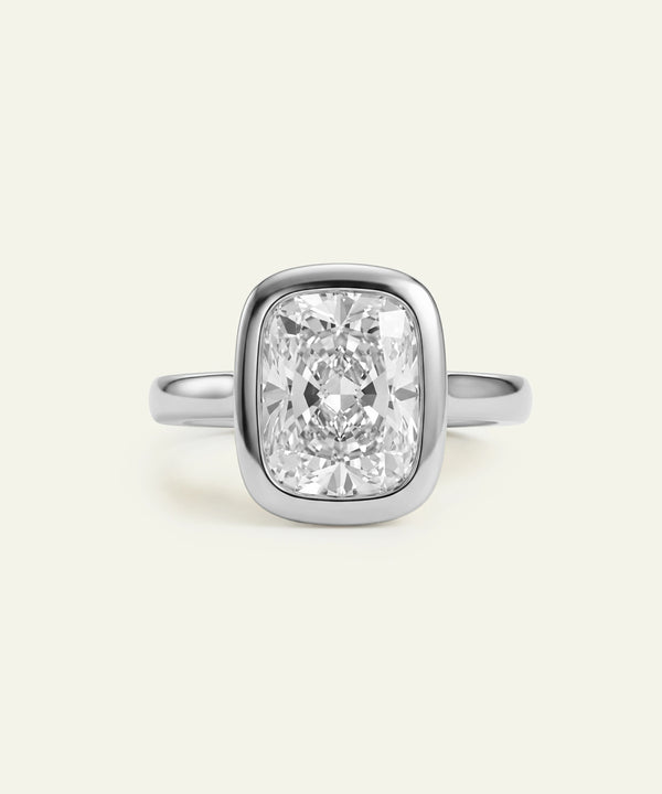 A cushion-cut diamond ring in a silver-toned setting on a light cream background.