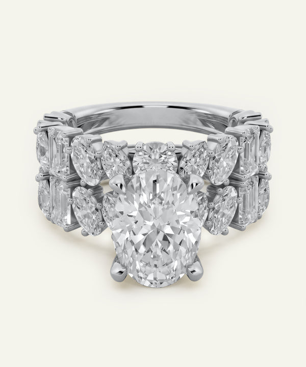 Oval-cut center diamond engagement ring in white metal, featuring a wide band adorned with marquise-cut and emerald-cut side diamonds in a symmetrical, multi-row design. The ring is shown from the front against a light neutral background.