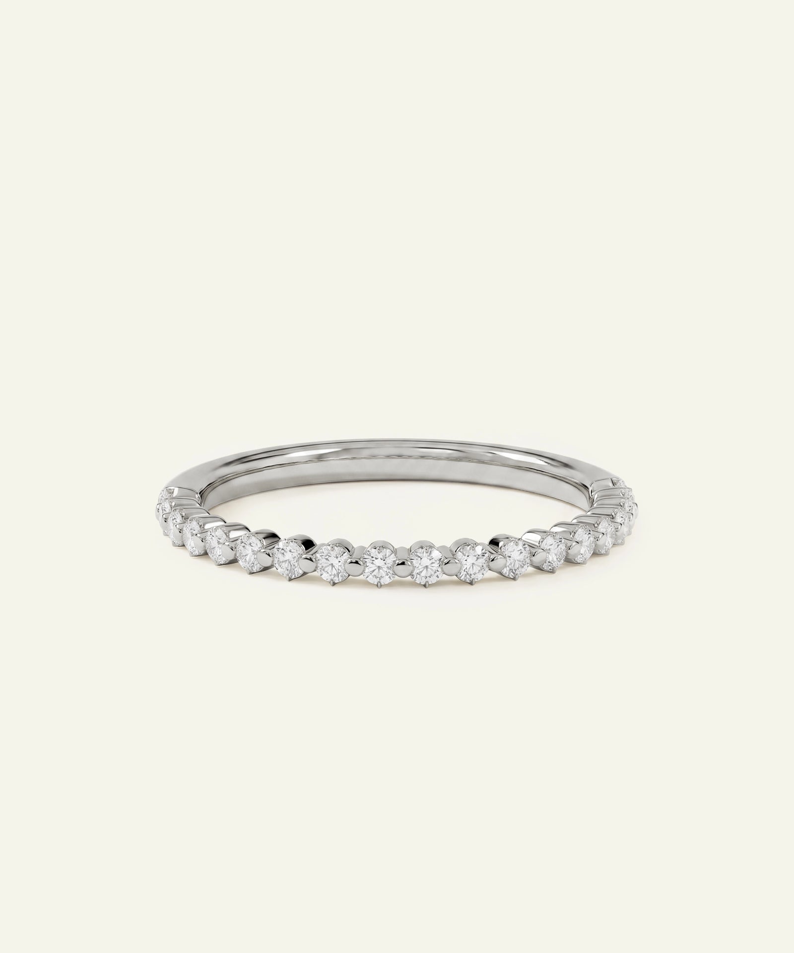 A thin silver band ring featuring a row of small, round-cut clear gemstones, photographed on a solid, warm off-white background.