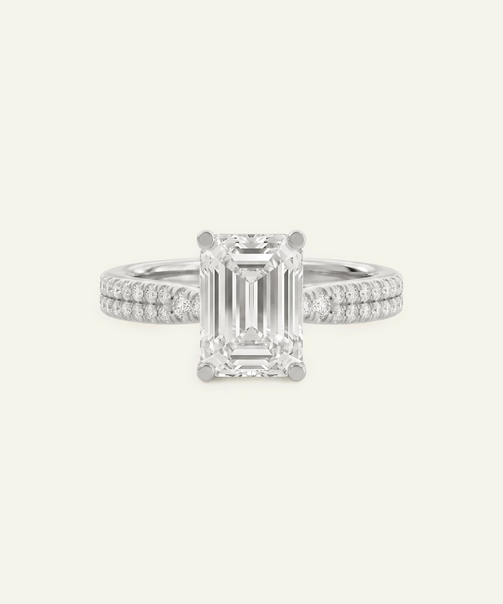 An emerald-cut diamond engagement ring with a silver-toned band paved with small diamonds, centered on a light cream background.