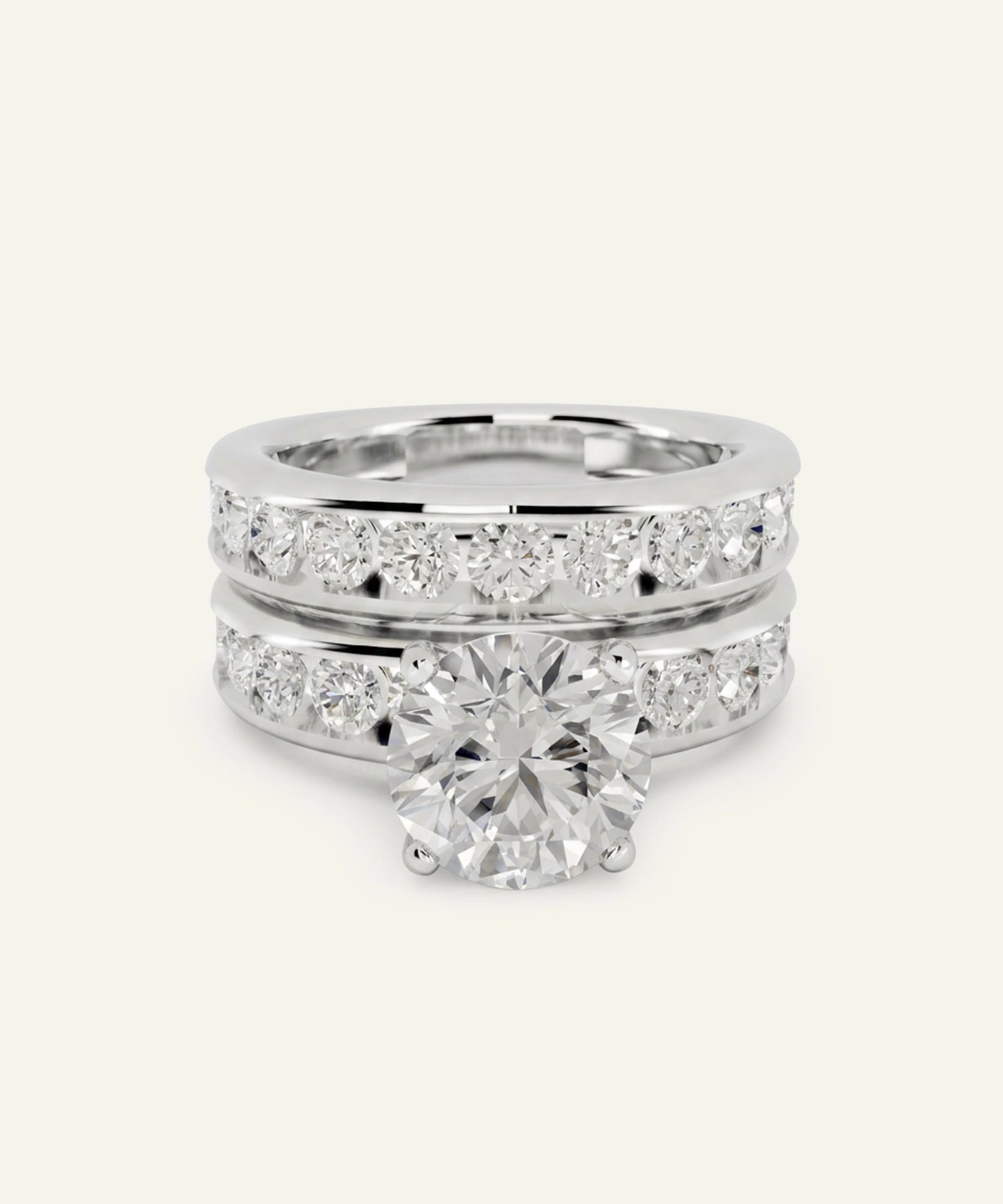 A three-stone diamond engagement and wedding band set in polished white gold or platinum, featuring a large round-cut center stone and smaller pavé diamonds, shown on a light cream background.