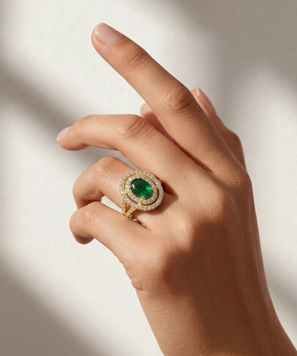 Hand wearing a gold ring with a green gemstone on a neutral background