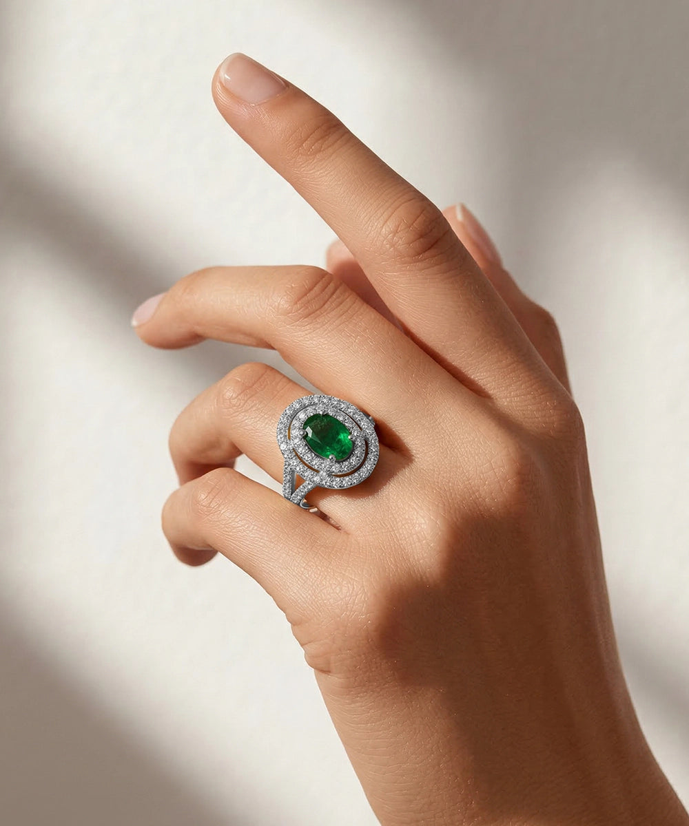 Hand wearing a ring with an emerald stone on a neutral background