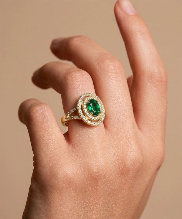 Gold ring with a green gemstone on a hand against a beige background
