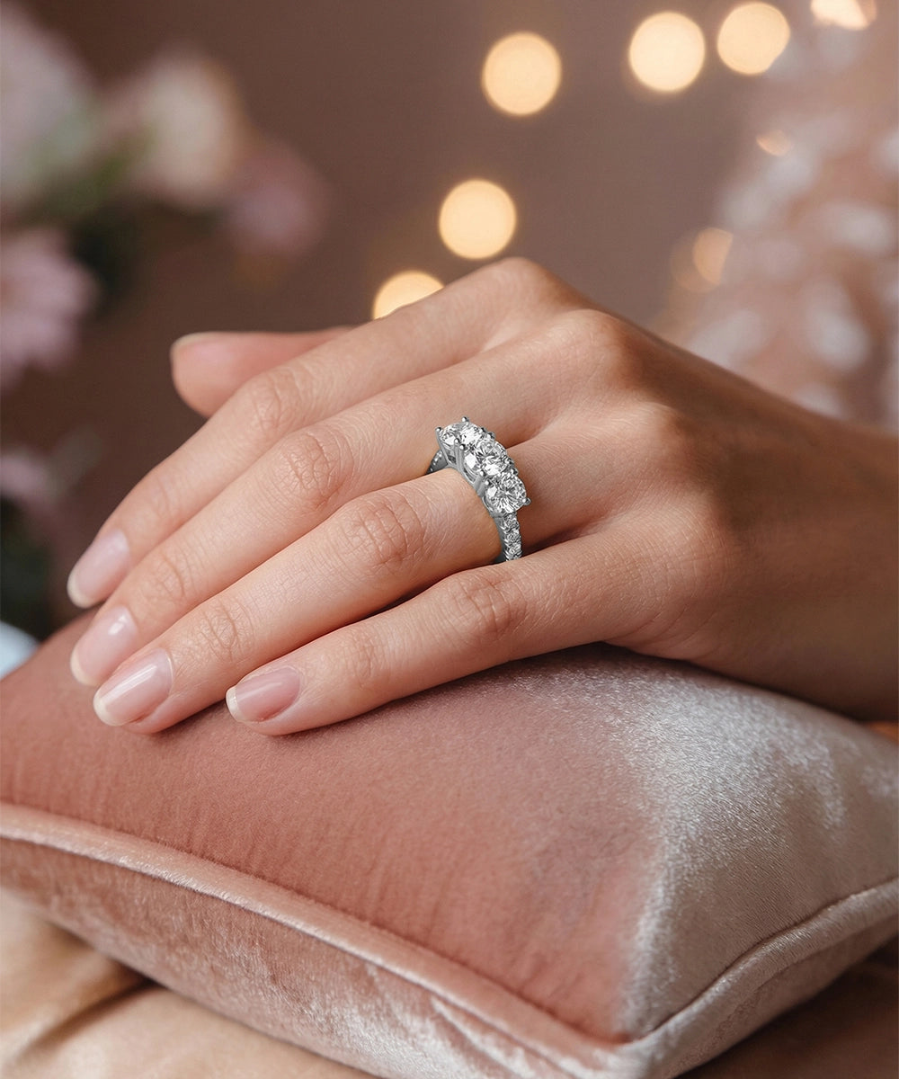 Hand wearing a diamond ring on a soft surface with blurred lights in the background