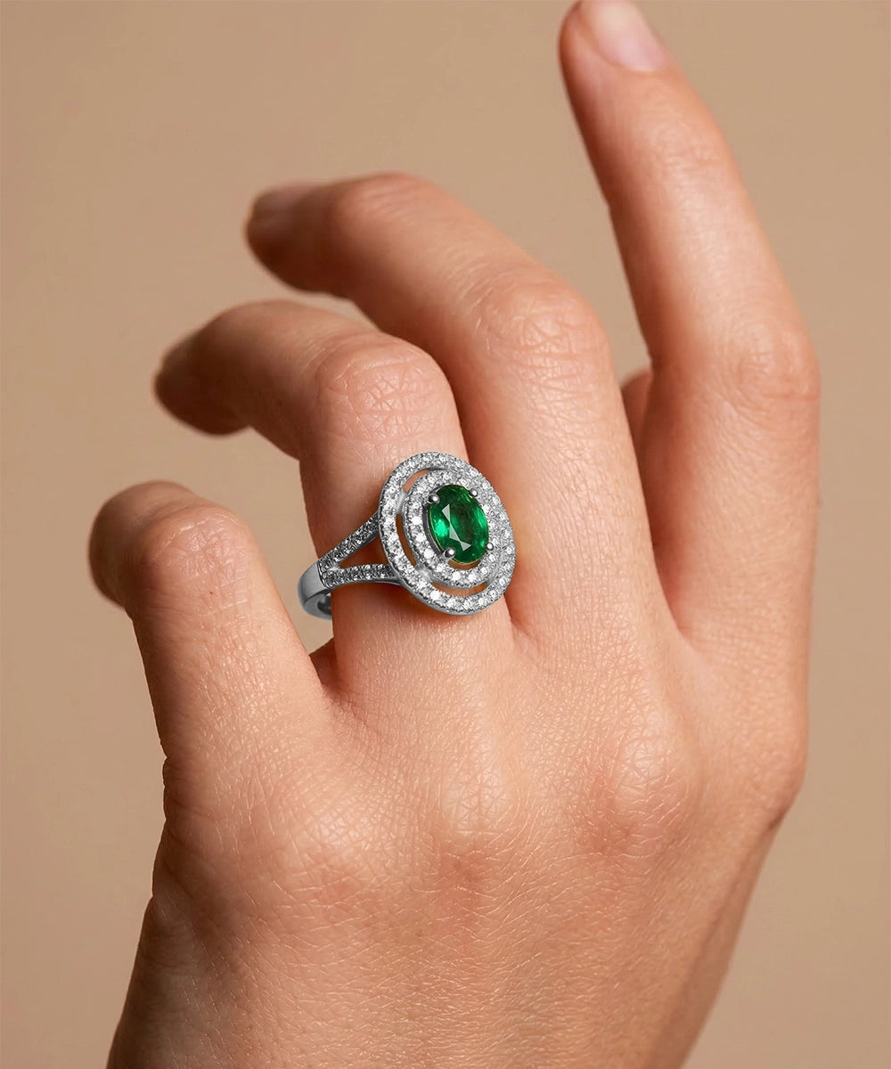 Ring with a green gemstone on a hand against a beige background