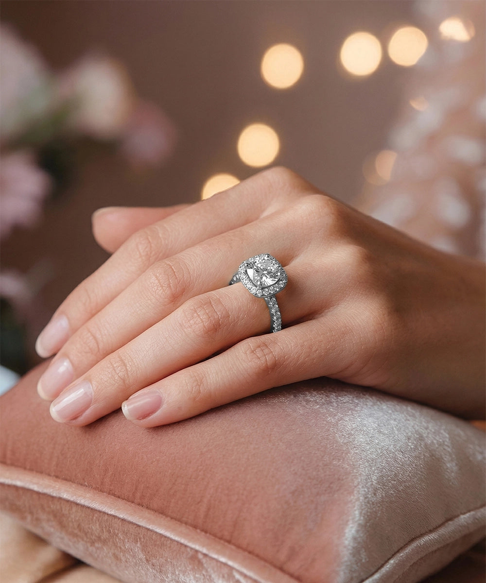 Hand wearing a diamond ring on a soft surface with blurred lights in the background