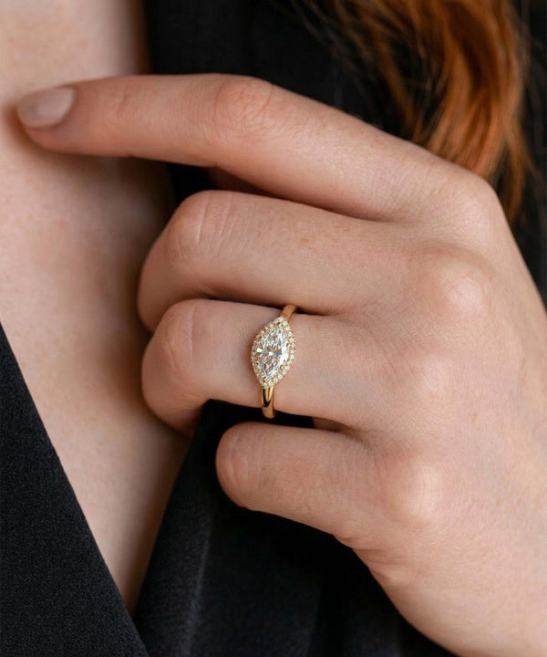 Close-up of a hand wearing a gold ring with a marquise-shaped diamond.