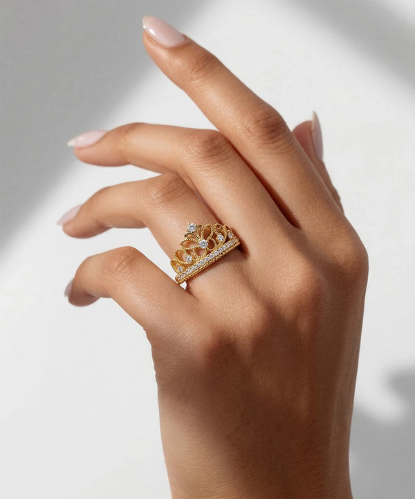 Hand wearing a gold ring with intricate design on a neutral background