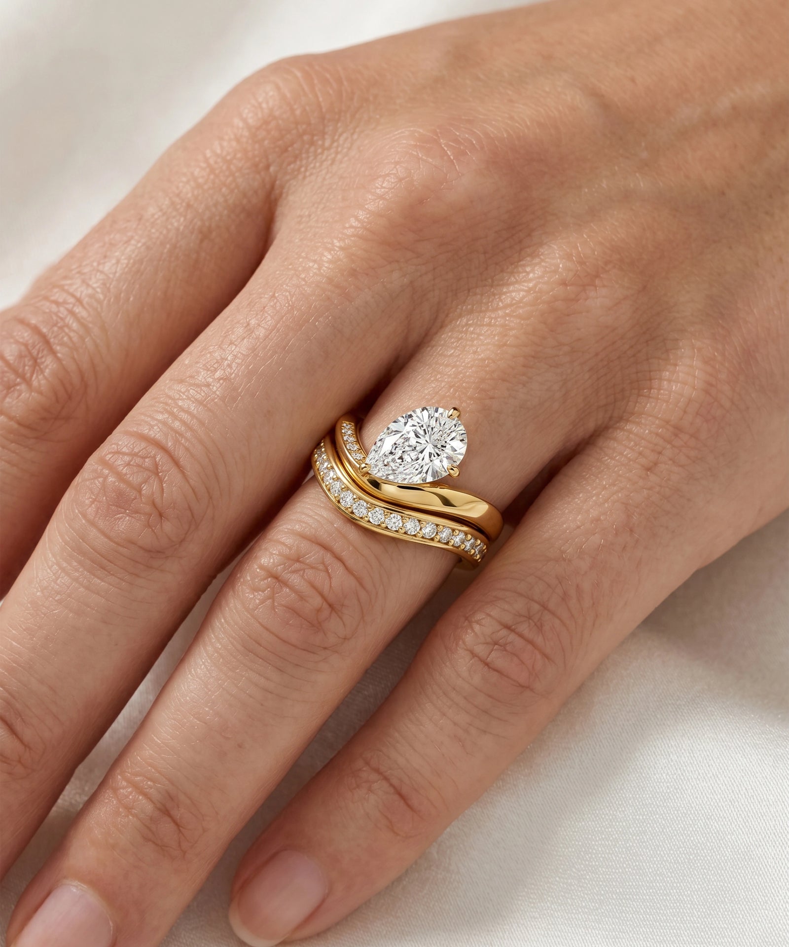 Gold ring with a diamond on a person's finger against a neutral background