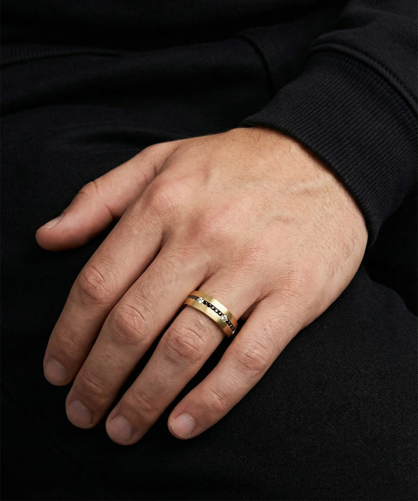 Hand wearing a gold ring with a black background