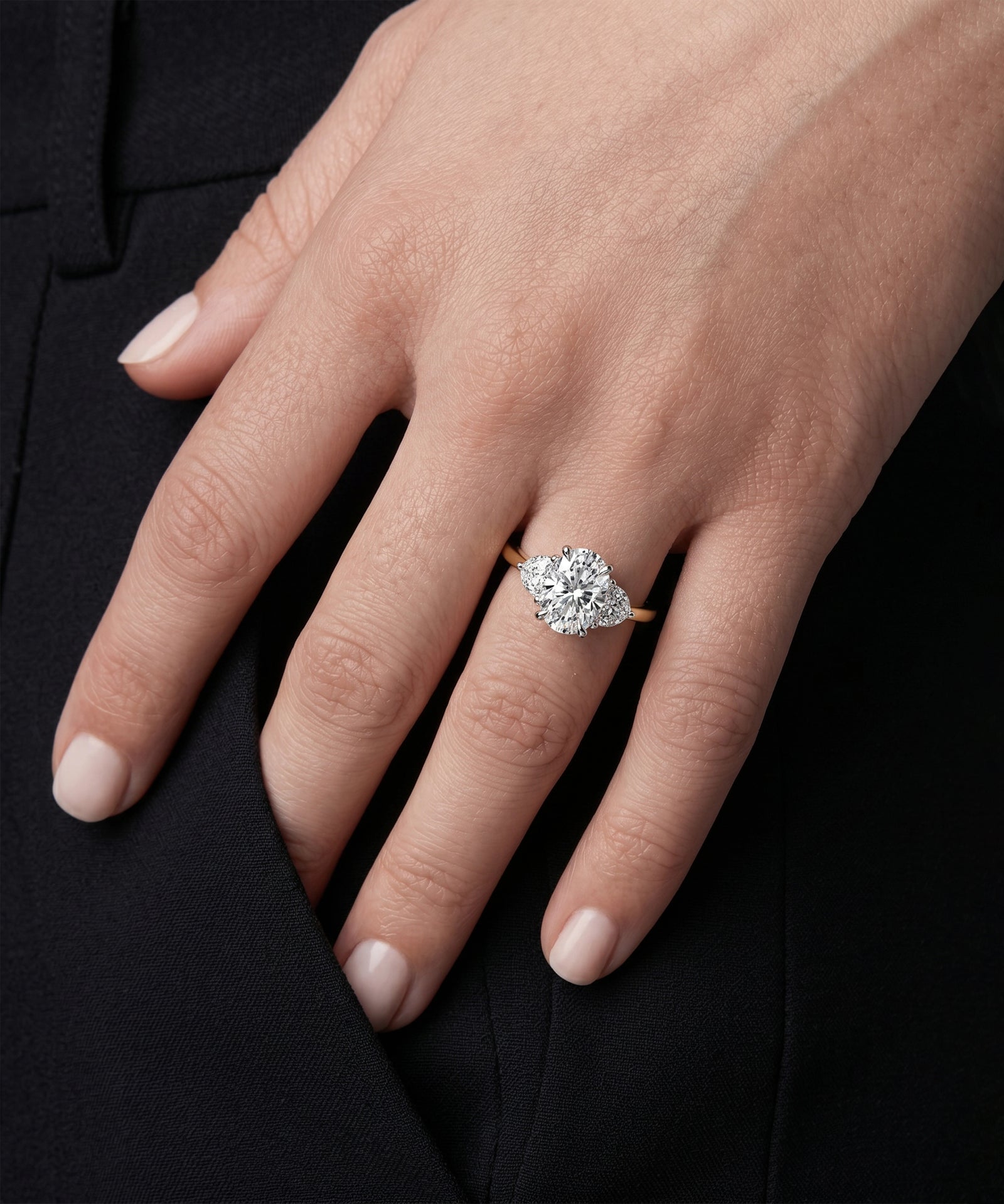 Three-stone oval diamond ring with a yellow gold band on a model's hand.